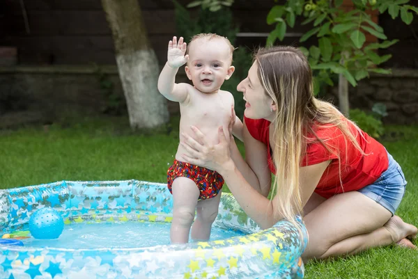 Baby boy playing with mom in swimming pool at garden