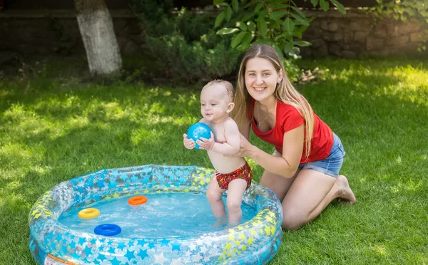 Smiling woman holding her baby boy in inflatable swimming pool a