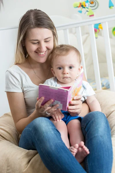 Portrait of cheerful mother reading book to her baby boy at livi