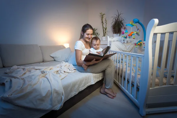 Adorable baby sitting on mothers lap and reading book before goi