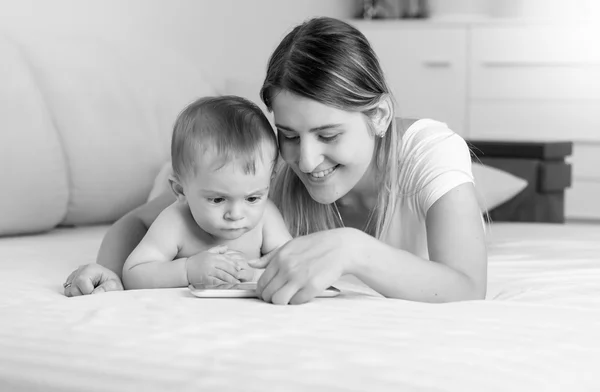 Black and white portrait of smiling mother and baby using tablet