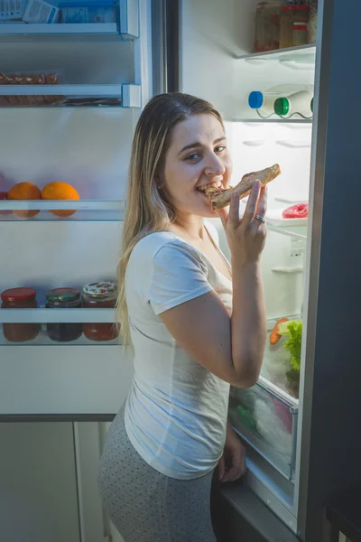 Young smiling woman eating pizza on kitchen at night