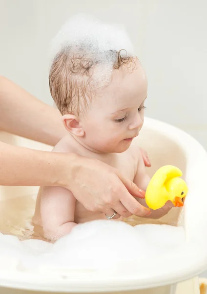 Cute baby boy playing in foam bath with yellow rubber duck