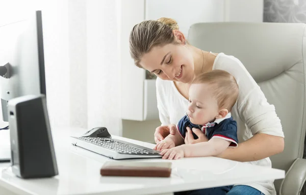 Young woman with baby working at home and using computer