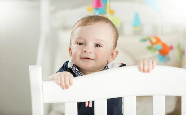 Smiling 9 month old baby standing in white wooden crib