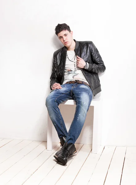 Man in jeans and leather jacket relaxing on white wooden chair
