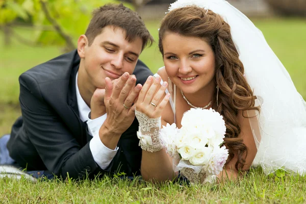 Newly married couple lying on grass and looking at wedding rings