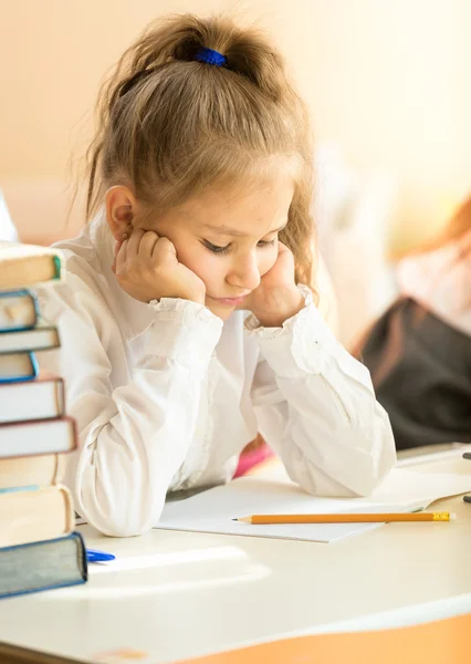 Portrait of upset schoolgirl looking at textbook with homework