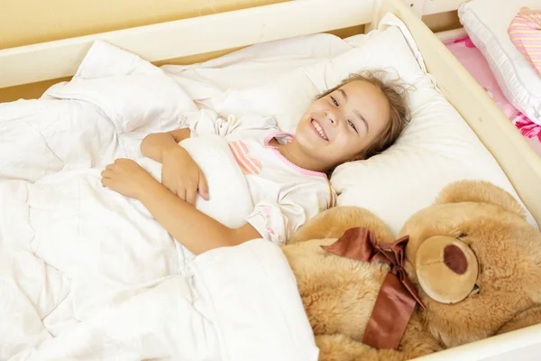 Smiling girl lying on bed with big teddy bear