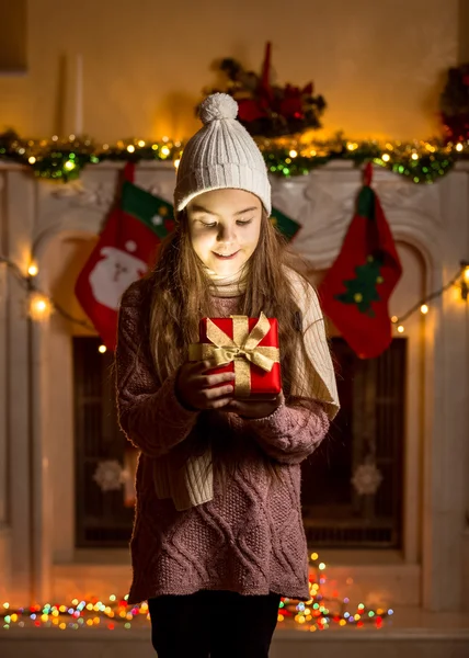 Girl in wool sweater and hat looking inside of glowing present b