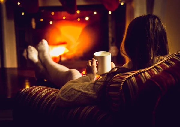 Toned photo of woman warming up with hot tea at fireplace