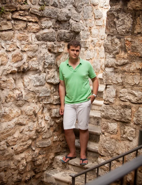 Man in shorts leaning against ancient stone wall