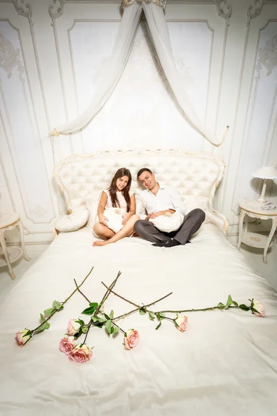 Couple in love sitting on luxurious bed decorated with roses