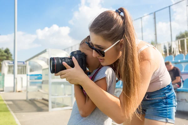 Woman teaching little girl to photograph using professional came