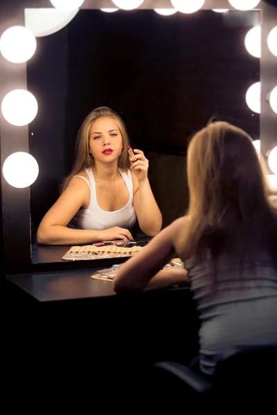 Blonde woman applying makeup at vintage theater mirror