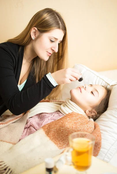 Caring mother spraying daughters nose lying in bed