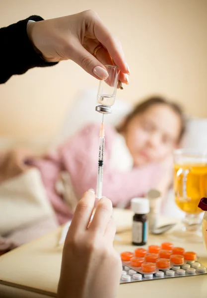 Young woman filling syringe from ampule next to child bed