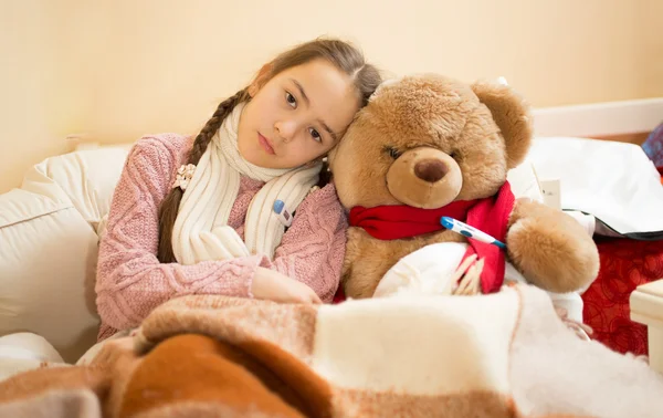Sad girl with flu lying in bed with teddy bear
