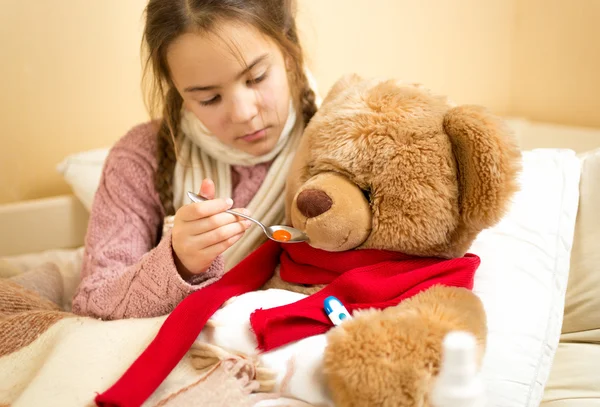 Little girl giving medicines to teddy bear