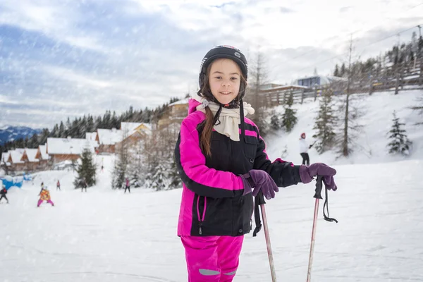 Smiling girl in ski suit posing with ski sticks on slope