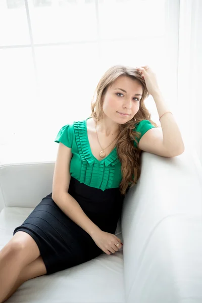 Beautiful young woman sitting on white couch next to window