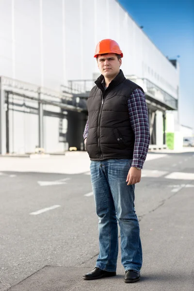 Full length portrait of engineer posing against big warehouse