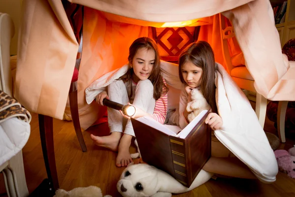 Two sisters sitting in house made of blankets and reading book