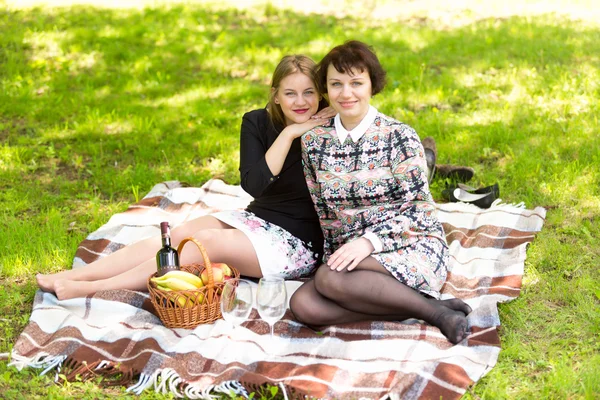 Two women relaxing on blanket at park and having picnic