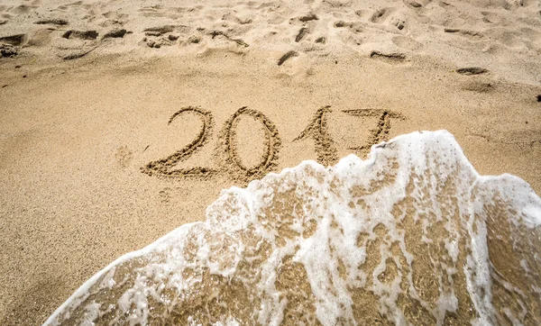 Closeup of 2017 written on sand being washed off by wave