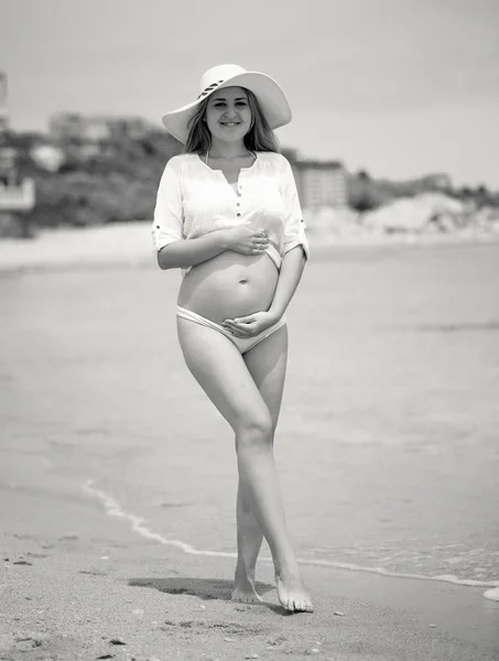 Toned photo of cute pregnant woman in hat posing on sea beach