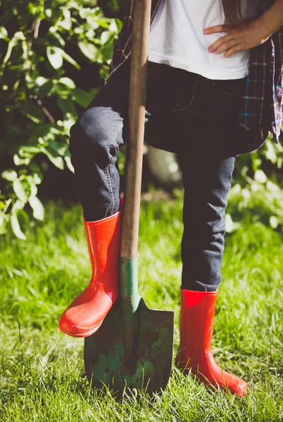 Toned photo of young woman holding leg in rubber boots on shovel