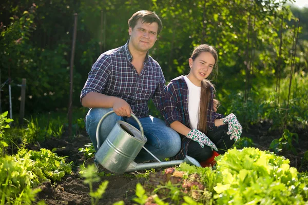 Smiling man and cute girl working at garden with watering can