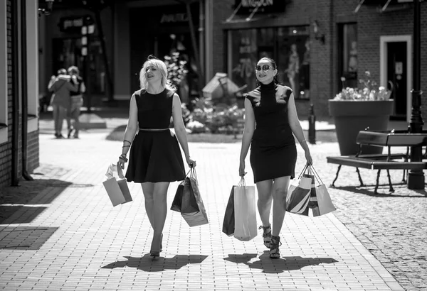 Black and white photo of two women walking with shopping bags