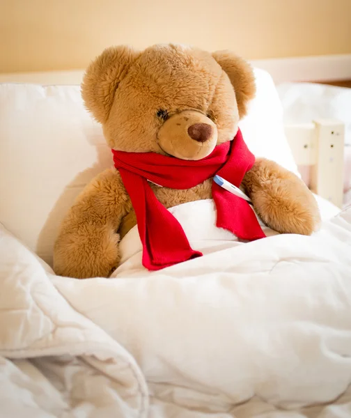 Closeup of teddy bear in red scarf lying in bed