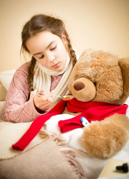 Little girl giving pills to sick teddy bear