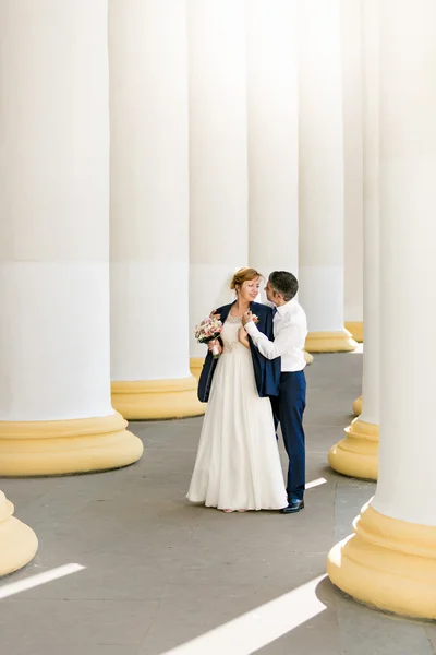 Newly married couple posing between high columns at sunny day