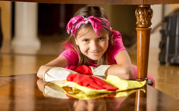 Smiling girl in rubber gloves cleaning table by rag