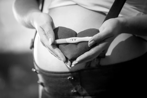 Black and white photo of pregnant woman holding pregnancy test
