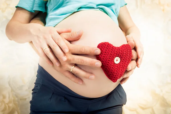 Caring and loving expectant parents holding red heart on abdomen
