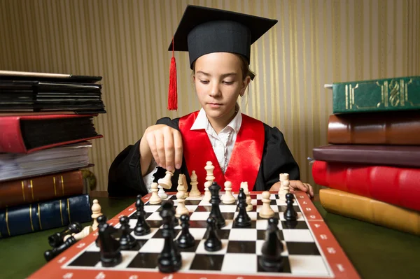 Portrait of smart girl in graduation cap playing chess