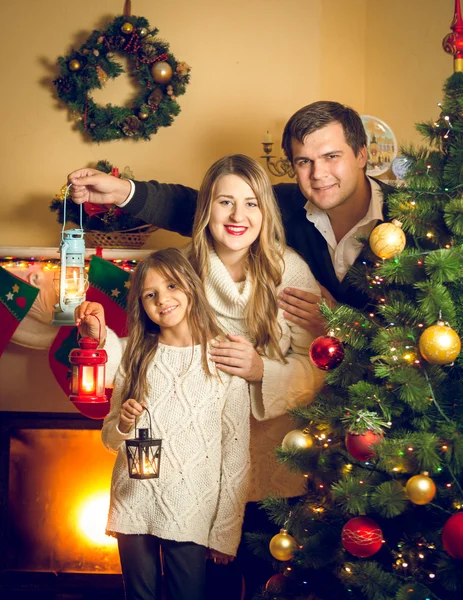 Portrait of happy family posing with lanterns at Christmas tree