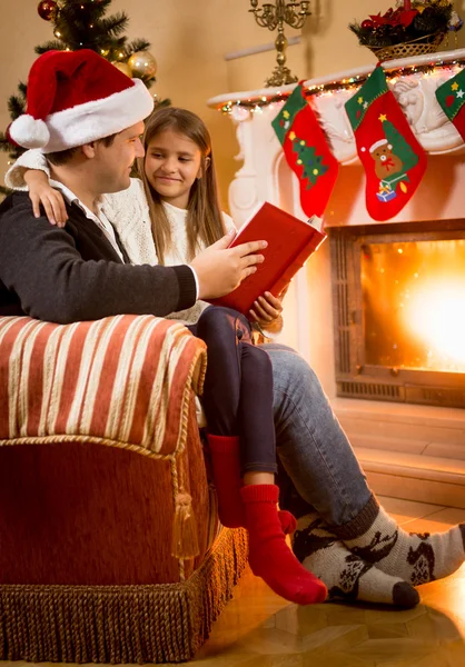 Father reading book to daughter sitting at fireplace