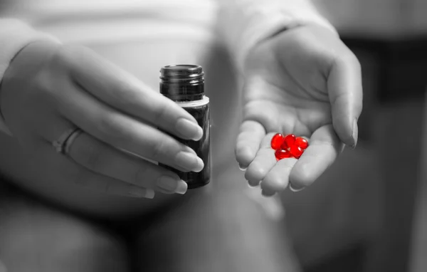 Black and white photo of pregnant woman holding red pill on hand