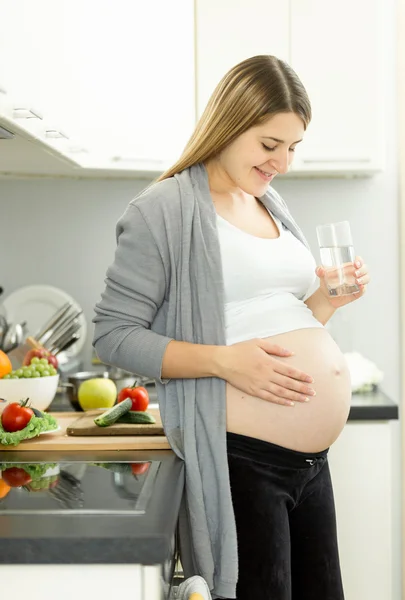 Pregnant woman on third trimester posing with glass of water on