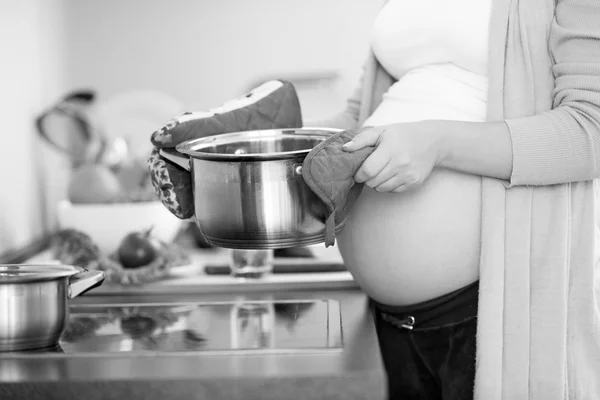 Black and white photo of pregnant woman holding metal pan on kit