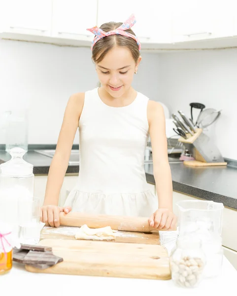 Cute girl rolling and kneading dough on wooden board