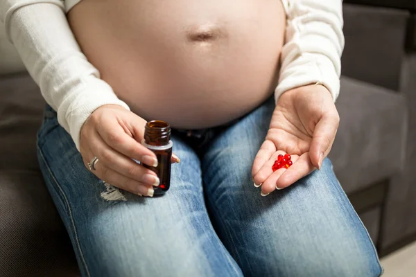 Closeup of pregnant woman on third trimester holding vitamins in