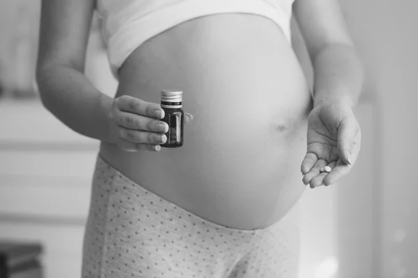 Black and white shot of pregnant woman holding vitamins in pills