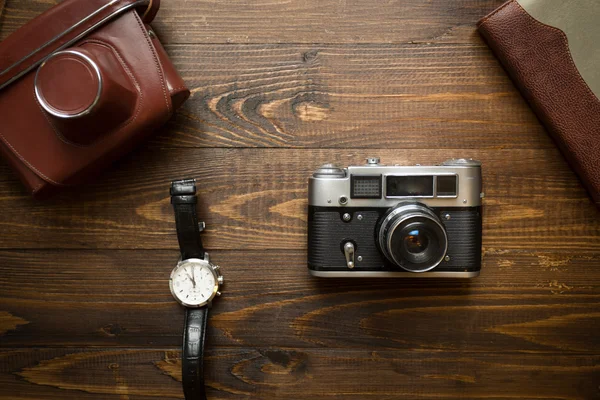 Top view of vintage camera, notebook and watches on wooden backg