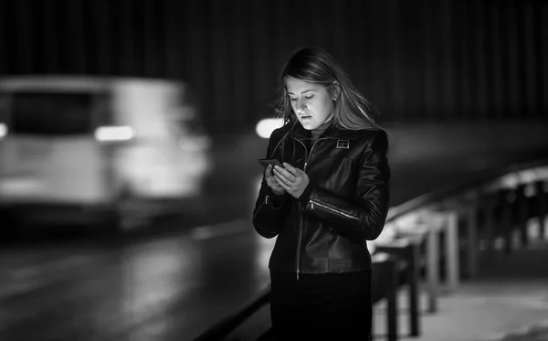 Black and white portrait of woman typing message on street at ni